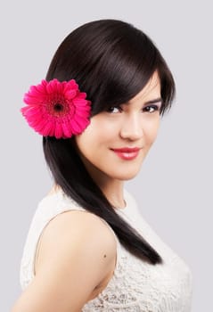 Portrait of a beautiful young woman with a flower in her hair isolated on grey
