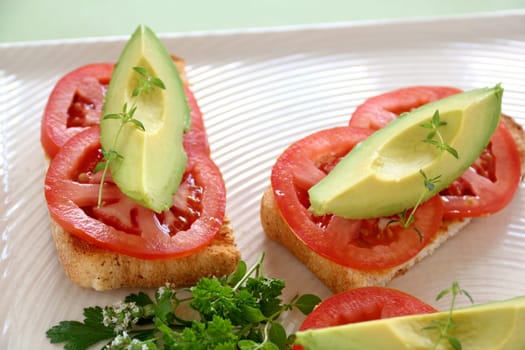 Delicious fresh slice of avocado with tomato and thyme on sliced toasts.