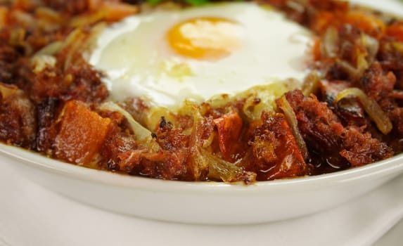 Baked corned beef hash with egg, tomato and onion with parsley.