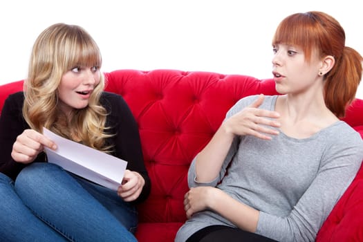 young beautiful blond and red haired girls on red sofa are excided about letter in front of white background