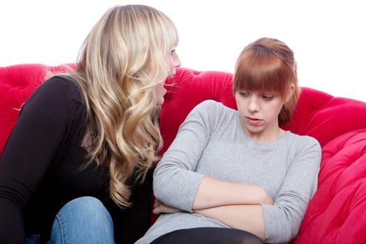 young beautiful blond and red haired girls on red sofa have a fight in front of white background