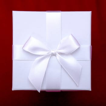 beautiful white gift box with ribbon on top of red sofa background