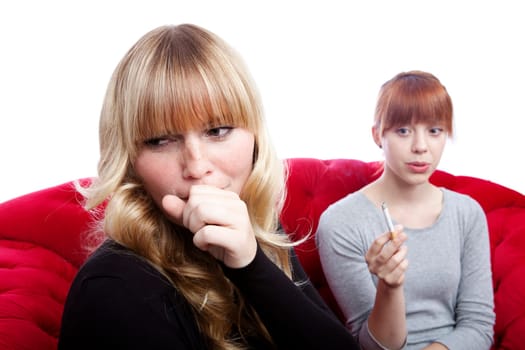 young beautiful blond and red haired girls on red sofa in front of white background