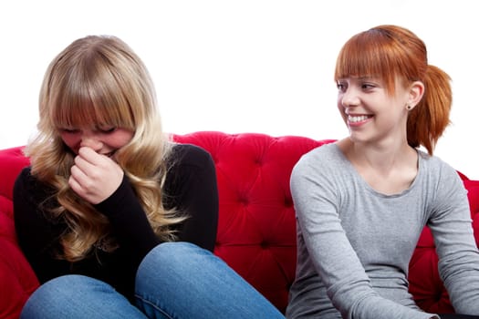 young beautiful blond and red haired girls talking and sitting on red sofa in front of white background