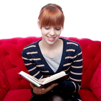young beautiful red haired girl on red sofa read a book in front of white background