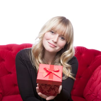 young blond haired girl has a present box for you on red sofa in front of white background