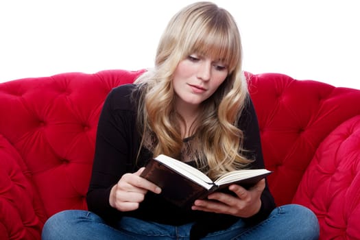 young blond haired girl on red sofa read a book in front of white background
