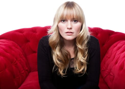 stunning young blond haired girl on red sofa in front of white background