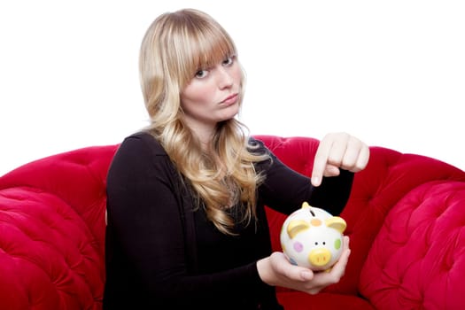 young blond haired girl want money in her piggybank on red sofa in front of white background