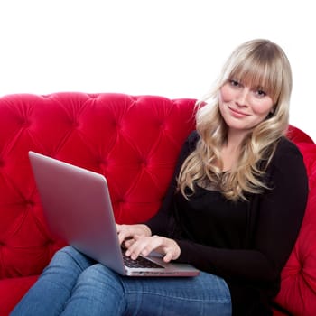 young blond haired girl on red sofa working with laptop in front of white background