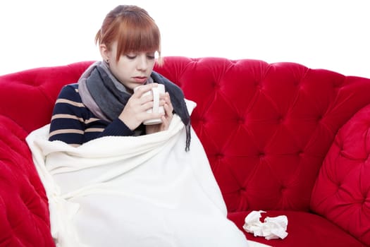 young beautiful red haired girl on red sofa has a cold in front of white background
