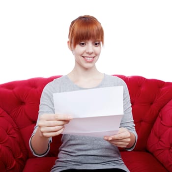 young beautiful red haired girl on red sofa reading a letter in front of white background