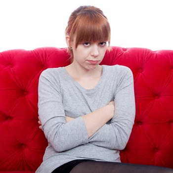 young beautiful red haired girl on red sofa is offended in front of white background