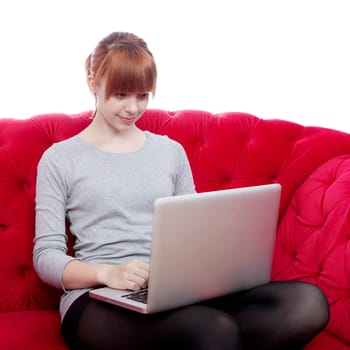 young beautiful red haired girl on red sofa working on laptop in front of white background