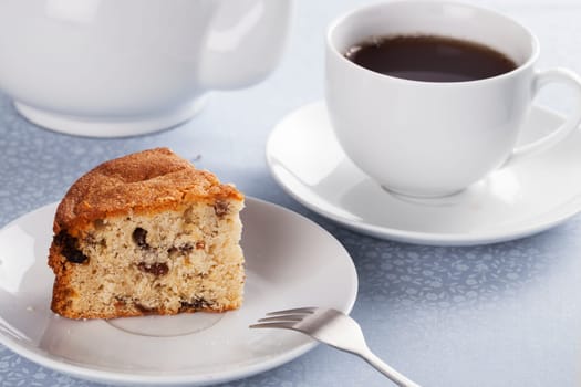 Slice of fruitcake made with raisins and cup of tea