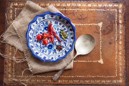 Cardamon seeds, star anise and peppers in a colorful blue bowl on a vintage table.