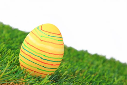 Colorful colored easter egg on artificial grass against white background