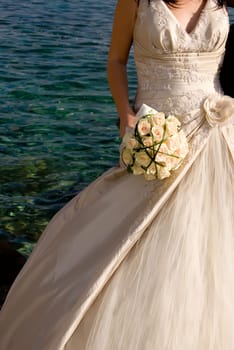 Bride holding wedding bouquet. Blue sea in the background.