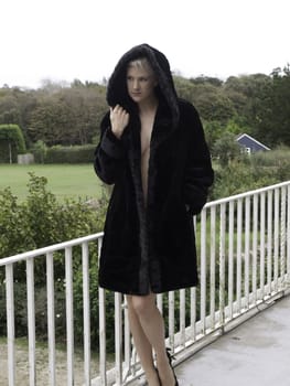 Beautifal blond only wearing a fur coat on balcony