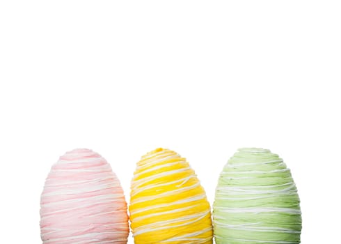 Fresh pastel handcrafted Easter Eggs covered in raffia or coloured straw standing in a row against a white background with copy space for your seasonal greeting