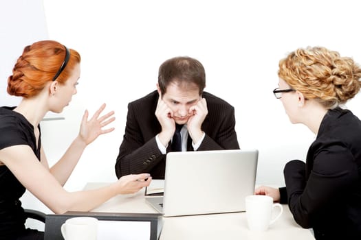 Business team in a serious meeting with the male leader staring dejectedly at his laptop while a female colleague explains something gesturing with her hands