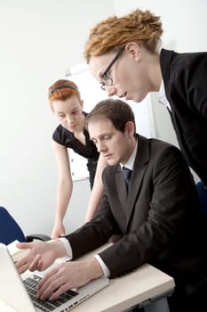 Three members of a business team brainstorming with the man gesturing towards his computer screen which they are all reading
