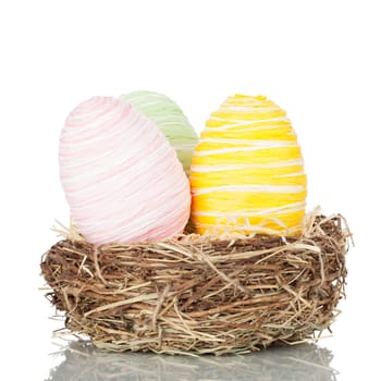 Three pastel coloured decorative Easter eggs in a nest. Studio shot over white background with reflection