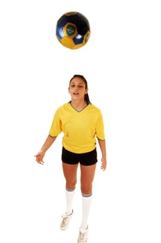 A pretty teenage girl standing in the studio in her soccer uniform and playing with the football, her hair in a ponytail for white background.