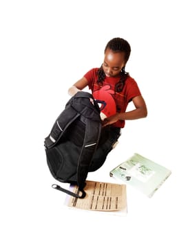 A young black school girl looking into her school backpack, kneeling on the floor and some books lying outside, for white background.