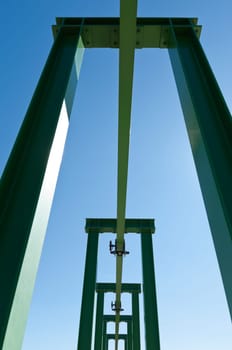 Detail of a small gantry crane painted green against the blue sky