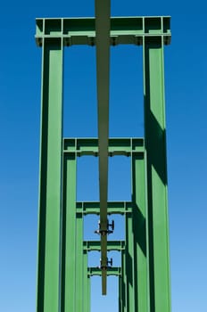 Detail of a small gantry crane painted green against the blue sky