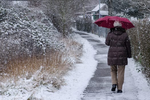Woman with red umbrella walking in snow and snowfall