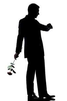 one caucasian man holding a rose flower  waiting checking time full length silhouette in studio isolated white background