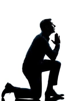 one caucasian man kneeling praying  full length silhouette in studio isolated white background