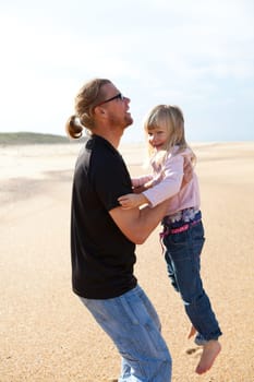 Father holding young daughter in arms at beach while on vacation in Portugal