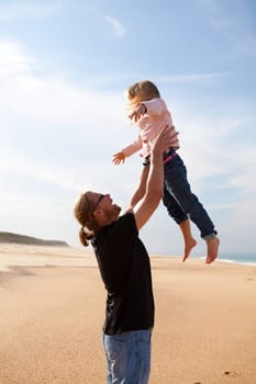 Father throwing young daughter into the air at beach while on vacation