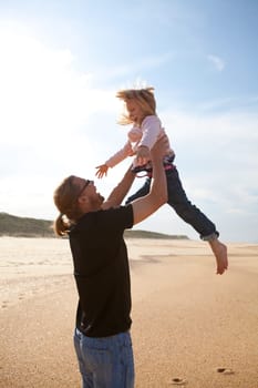 Father throwing young daughter into the air at beach while on vacation