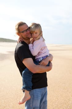 Father holding young daughter in arms at beach while on vacation in Portugal