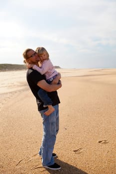 Father holding young daughter in arms at beach while on vacation in Portugal