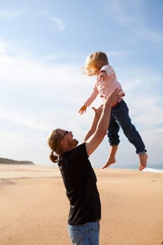 Father throwing young daughter into the air at beach while on vacation