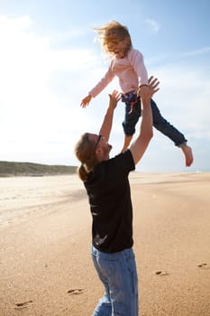 Father throwing young daughter into the air at beach while on vacation