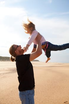 Father throwing young daughter into the air at beach while on vacation