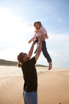 Father throwing young daughter into the air at beach while on vacation