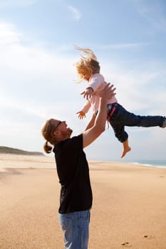 Father throwing young daughter into the air at beach while on vacation
