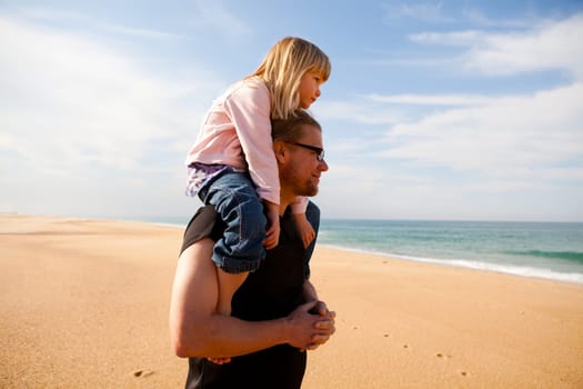 Father carrying young daughter piggyback on shoulders at beach