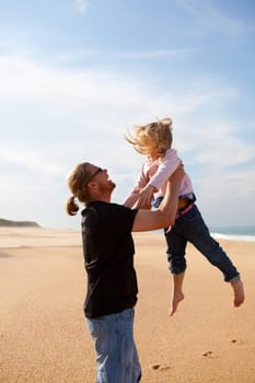 Father throwing young daughter into the air at beach while on vacation