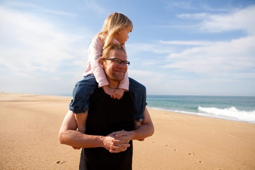 Father carrying young daughter piggyback on shoulders at beach
