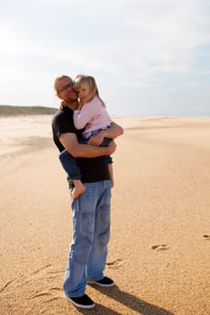 Father holding young daughter in arms at beach while on vacation in Portugal