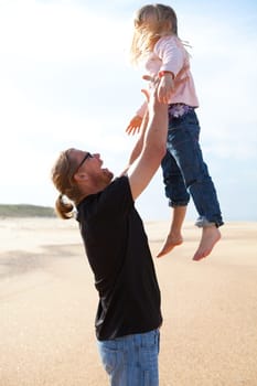 Father throwing young daughter into the air at beach while on vacation