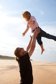 Father throwing young daughter into the air at beach while on vacation